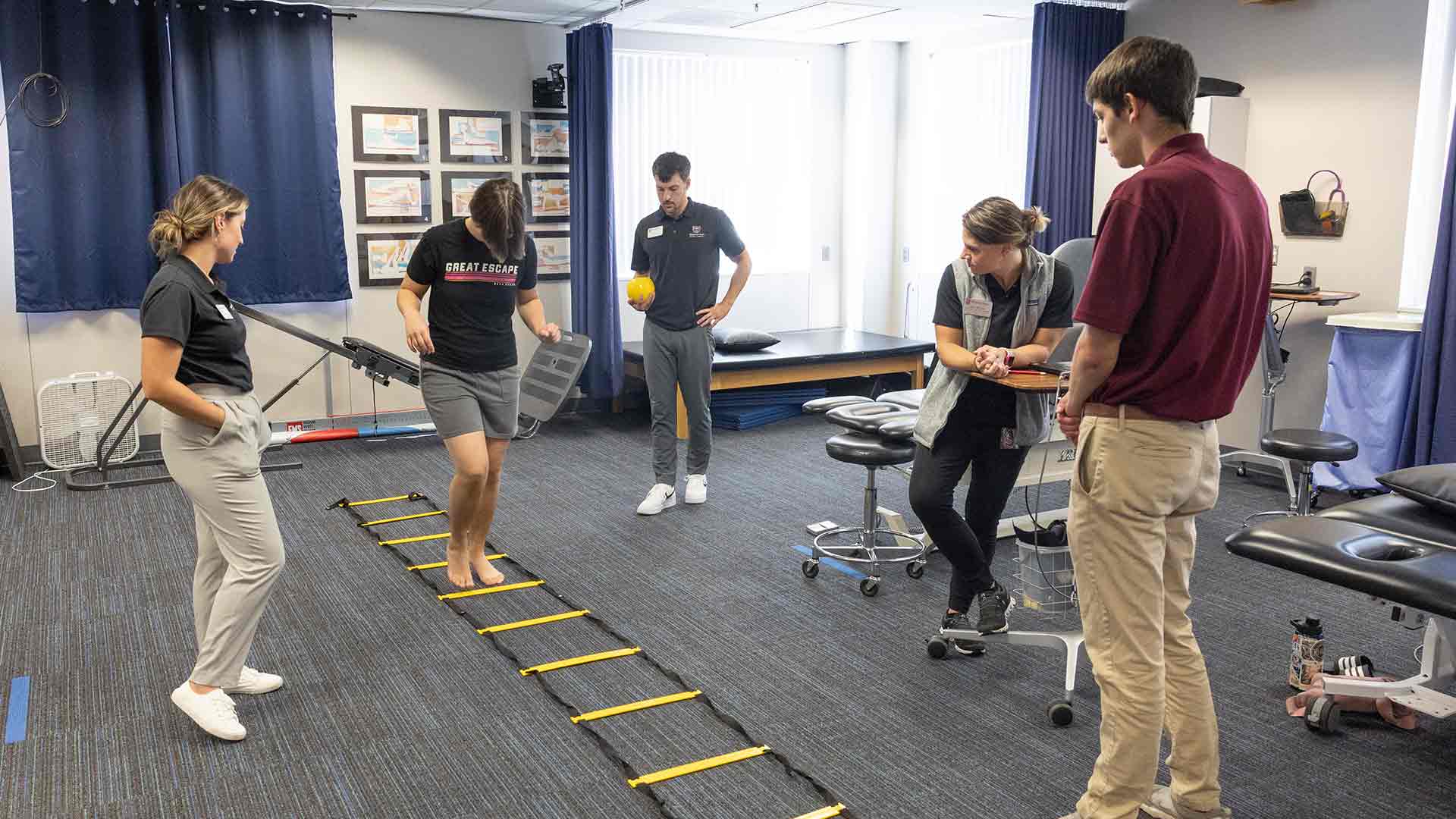 Physical therapy students and a professor guiding a young client through a rehab activity.